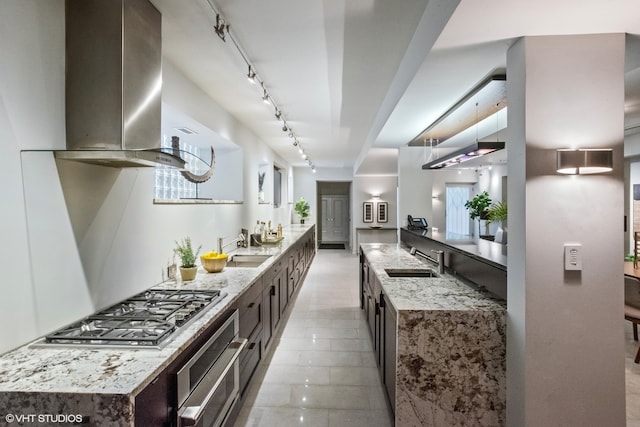 kitchen featuring wall chimney range hood, appliances with stainless steel finishes, rail lighting, sink, and light tile floors