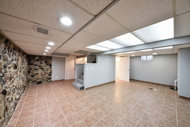 basement with a paneled ceiling and light tile floors