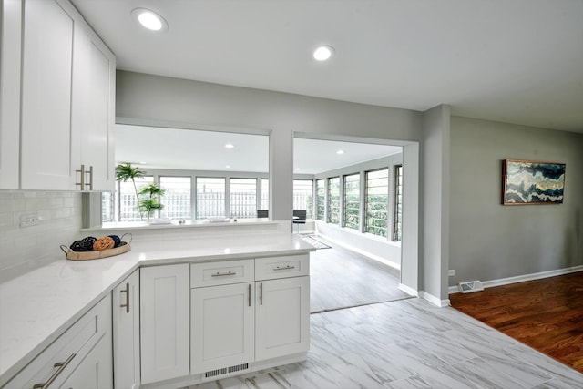 kitchen with white cabinets, light stone countertops, tasteful backsplash, and light hardwood / wood-style flooring