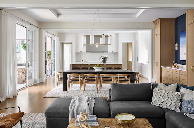 living room with a notable chandelier, light hardwood / wood-style floors, and a raised ceiling