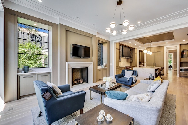 living room with a raised ceiling, ornamental molding, a chandelier, and light hardwood / wood-style flooring