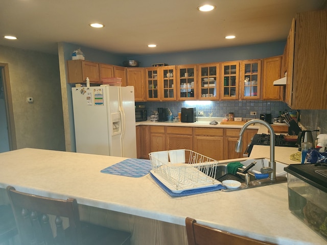 kitchen featuring white refrigerator with ice dispenser, backsplash, and sink