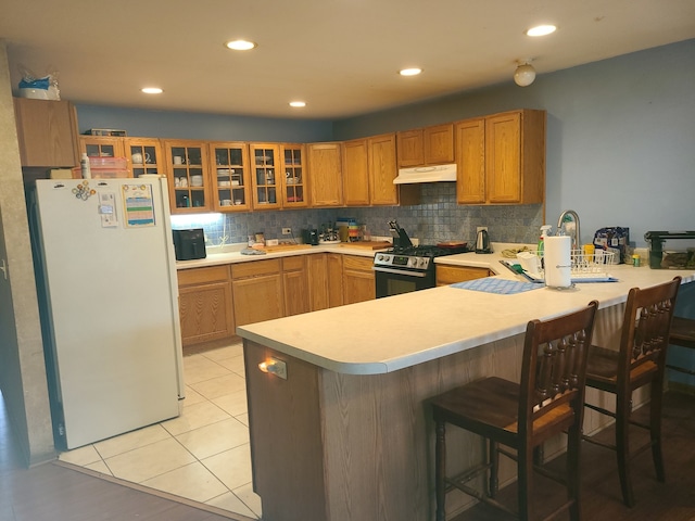 kitchen with gas range, white fridge, a breakfast bar area, and tasteful backsplash