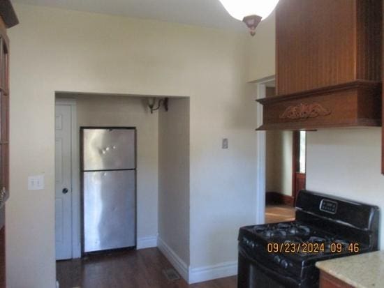 kitchen with black gas range, stainless steel fridge, dark hardwood / wood-style flooring, and premium range hood