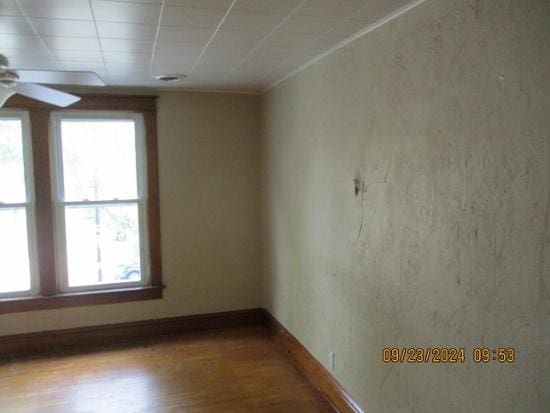 empty room featuring ceiling fan, plenty of natural light, wood-type flooring, and a drop ceiling