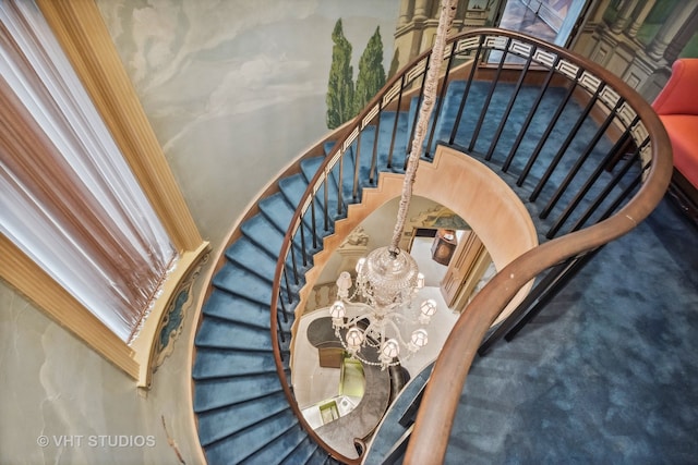 staircase featuring a high ceiling, dark colored carpet, and an inviting chandelier