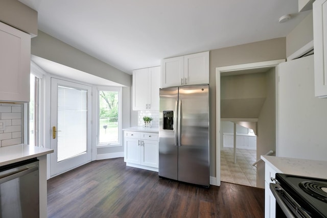 kitchen with white cabinets, dark tile floors, stainless steel appliances, light stone countertops, and backsplash