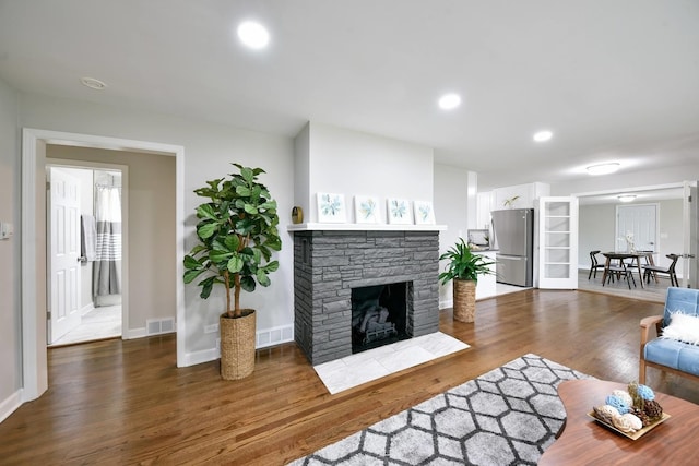 living room featuring a stone fireplace and dark wood-type flooring