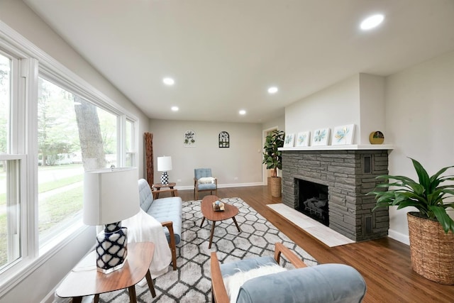 living room with plenty of natural light, a stone fireplace, and dark hardwood / wood-style flooring