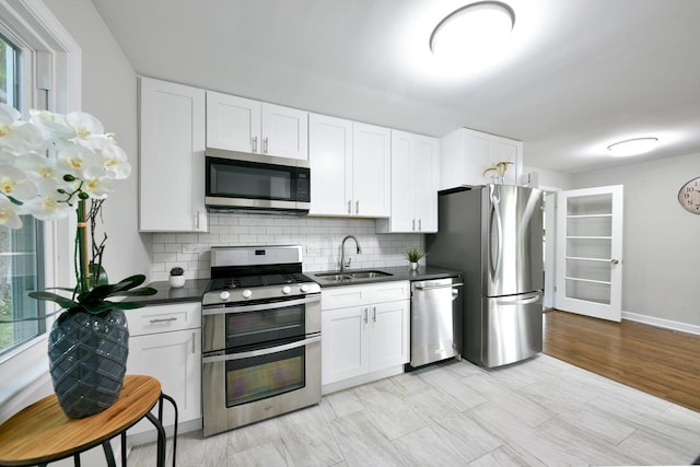 kitchen with stainless steel appliances, tasteful backsplash, white cabinetry, light wood-type flooring, and sink