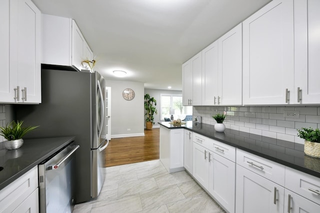 kitchen with tasteful backsplash, white cabinetry, stainless steel dishwasher, light tile floors, and dark stone countertops