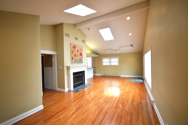 unfurnished living room with a baseboard radiator, light wood-type flooring, beamed ceiling, track lighting, and a skylight