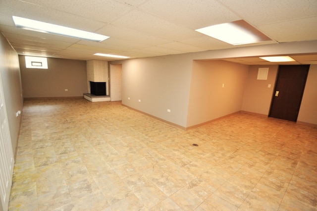 basement with a fireplace, light tile floors, and a drop ceiling