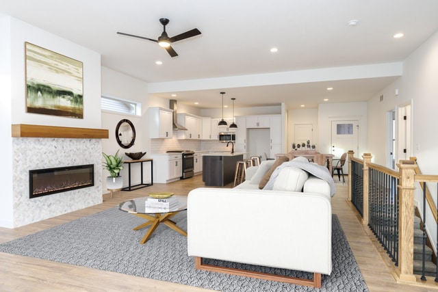 living room with a tile fireplace, ceiling fan, sink, and light wood-type flooring