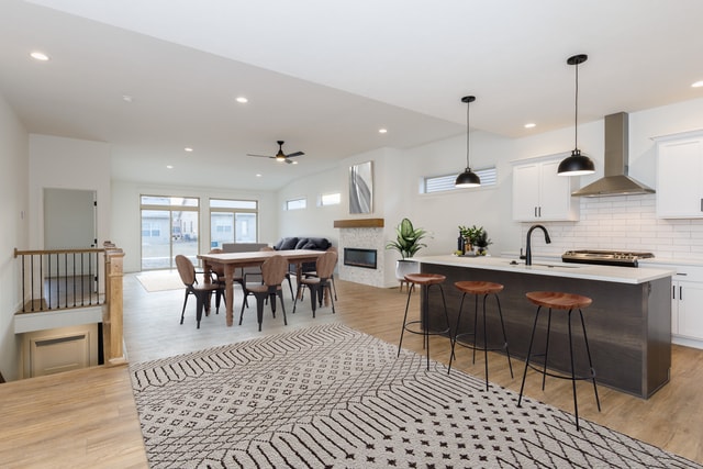 kitchen featuring a center island with sink, white cabinets, hanging light fixtures, wall chimney exhaust hood, and ceiling fan