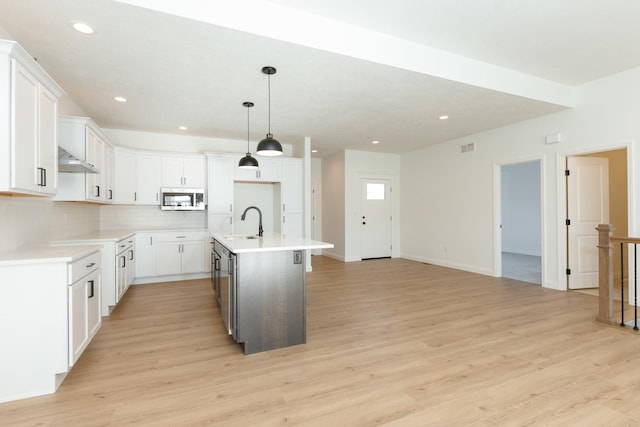 kitchen featuring ventilation hood, a kitchen island with sink, sink, decorative light fixtures, and white cabinets