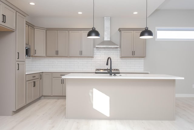 kitchen featuring ventilation hood, backsplash, a center island with sink, and hanging light fixtures