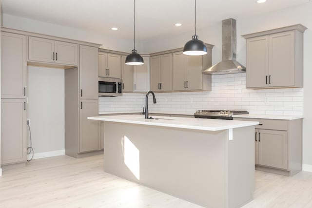 kitchen featuring appliances with stainless steel finishes, sink, wall chimney range hood, pendant lighting, and a center island with sink