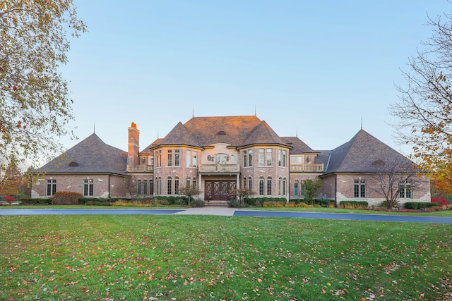 french country style house with a balcony and a front lawn