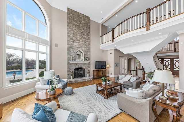 living room featuring a towering ceiling, light hardwood / wood-style flooring, and a stone fireplace