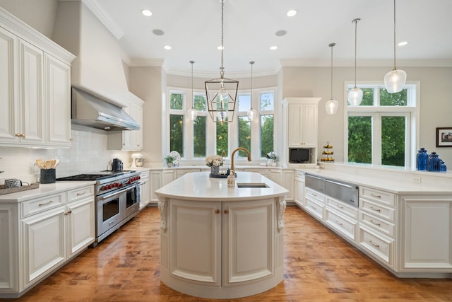 kitchen with a center island with sink, range with two ovens, hanging light fixtures, and sink