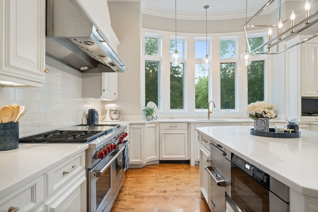 kitchen with exhaust hood, hanging light fixtures, sink, designer stove, and white cabinetry