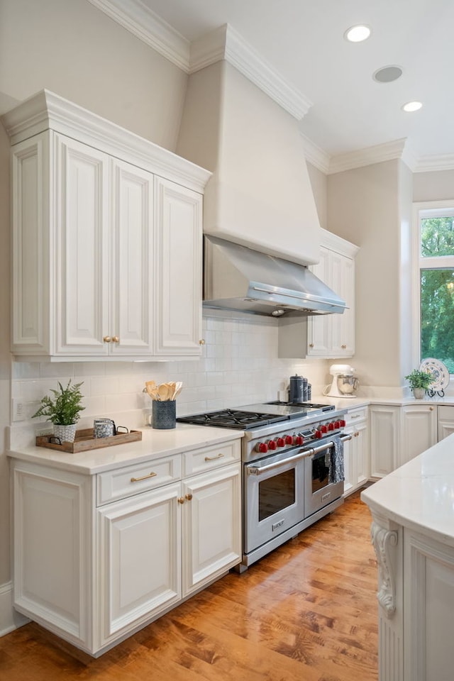 kitchen featuring white cabinetry, wall chimney range hood, light hardwood / wood-style flooring, range with two ovens, and decorative backsplash