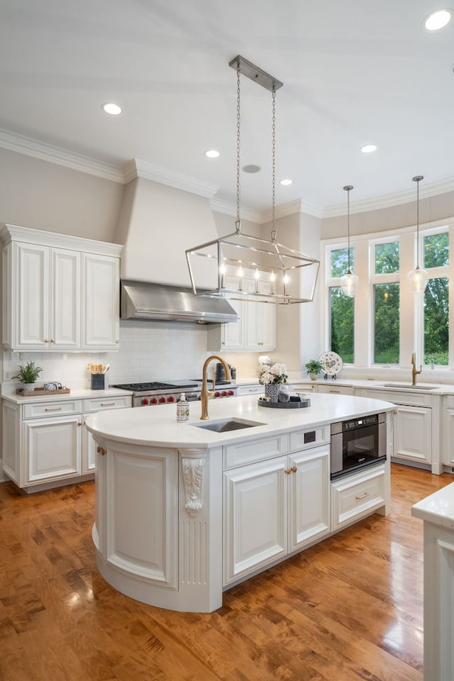 kitchen featuring backsplash, exhaust hood, white cabinets, an island with sink, and light hardwood / wood-style floors