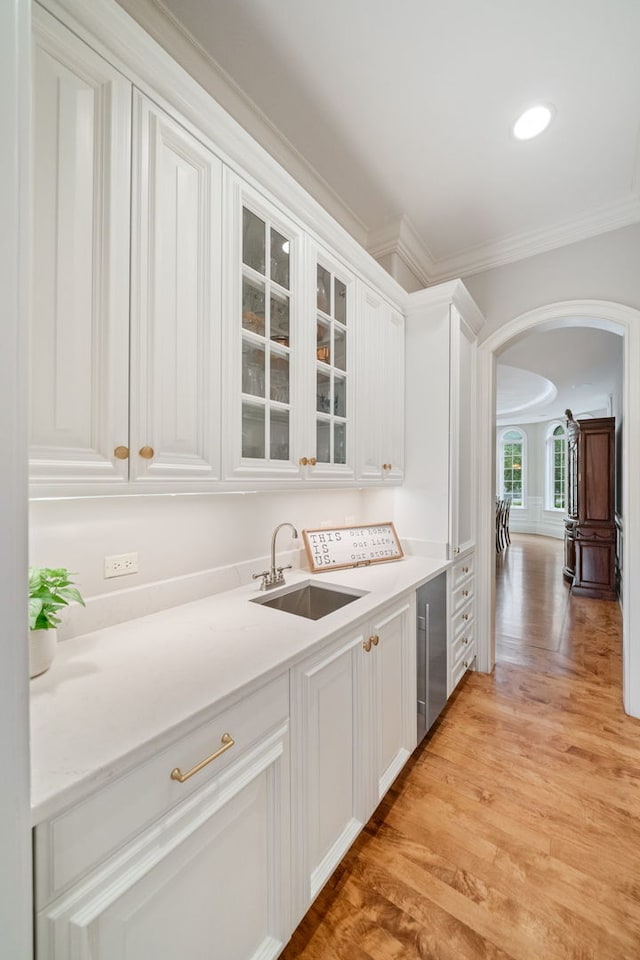 bar featuring light hardwood / wood-style floors, crown molding, white cabinetry, and sink