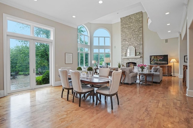 dining room featuring a fireplace, a high ceiling, light wood-type flooring, and ornamental molding