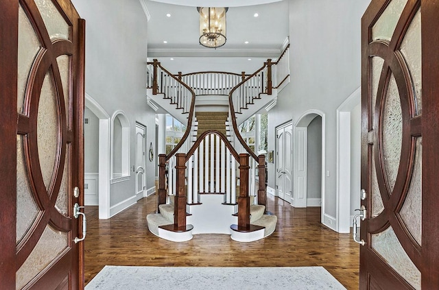 entryway featuring ornamental molding, a towering ceiling, dark wood-type flooring, and an inviting chandelier