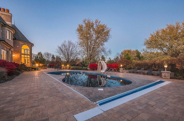 pool at dusk with a patio and a water slide