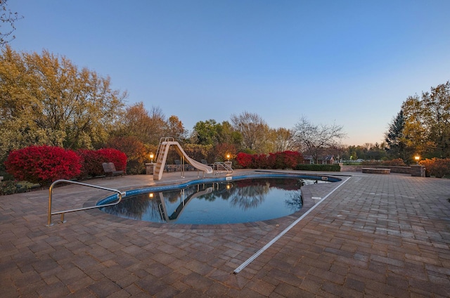 pool at dusk featuring a patio area and a water slide