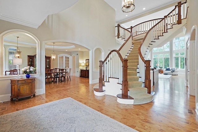 foyer entrance featuring a towering ceiling, light wood-type flooring, a notable chandelier, and ornamental molding