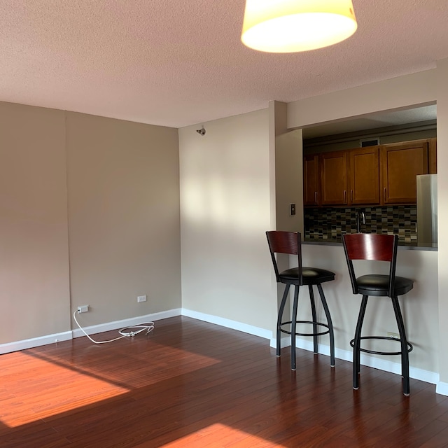 kitchen with backsplash, stainless steel refrigerator, a breakfast bar area, and dark hardwood / wood-style flooring