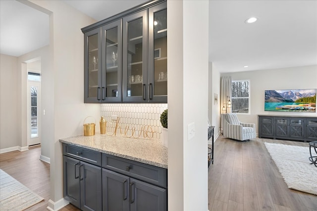 bar with light stone countertops, gray cabinetry, tasteful backsplash, and hardwood / wood-style flooring