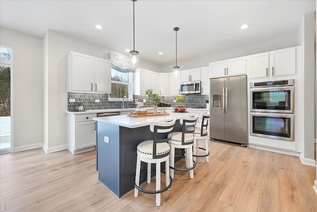 kitchen with pendant lighting, light hardwood / wood-style floors, a kitchen island, a kitchen bar, and appliances with stainless steel finishes