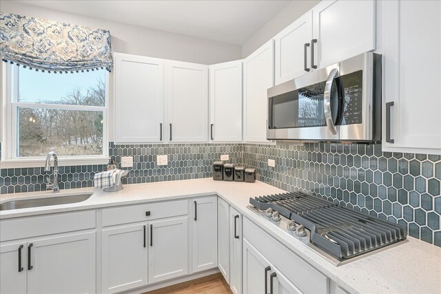 kitchen with appliances with stainless steel finishes, white cabinetry, backsplash, and sink