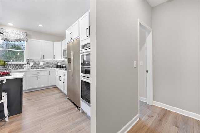 kitchen featuring white cabinetry, backsplash, stainless steel appliances, and light wood-type flooring