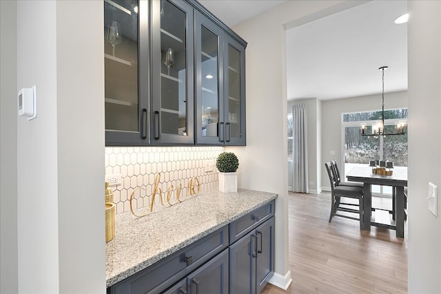 bar featuring hanging light fixtures, light stone countertops, tasteful backsplash, a notable chandelier, and light wood-type flooring