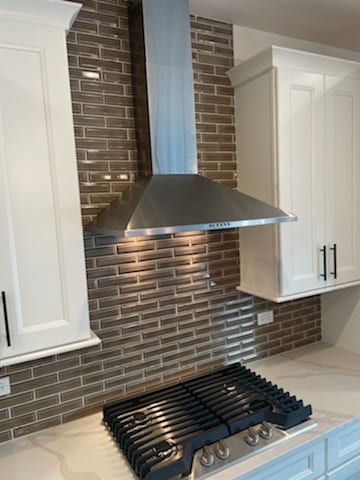 kitchen with tasteful backsplash, light stone counters, white cabinetry, and wall chimney range hood