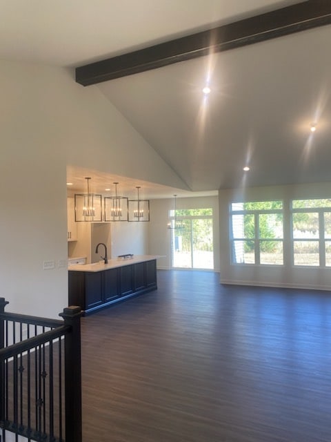 unfurnished living room with dark wood-type flooring, beamed ceiling, a notable chandelier, high vaulted ceiling, and sink