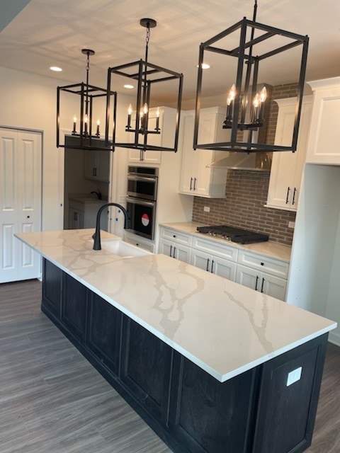 kitchen with dark hardwood / wood-style flooring, pendant lighting, an inviting chandelier, and an island with sink