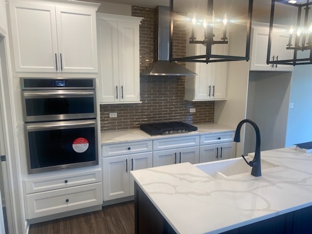 kitchen with white cabinets, wall chimney range hood, hanging light fixtures, and stainless steel appliances