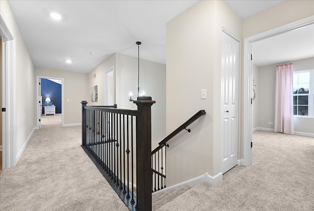 hallway featuring an inviting chandelier and light colored carpet