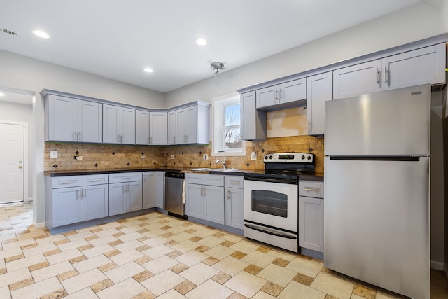 kitchen with appliances with stainless steel finishes, backsplash, gray cabinets, and light tile flooring