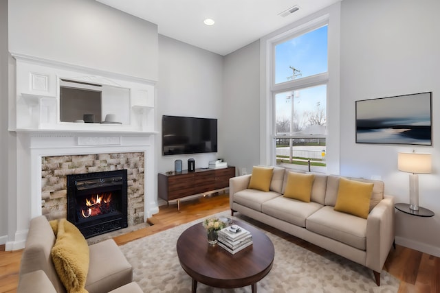 living room with a stone fireplace and light wood-type flooring