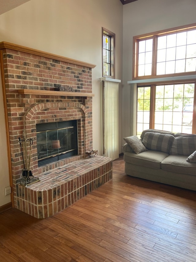 living room featuring a towering ceiling, a brick fireplace, and dark hardwood / wood-style floors