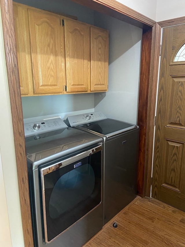 clothes washing area with cabinets, hardwood / wood-style floors, and washing machine and clothes dryer