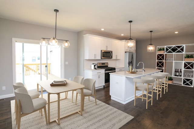 kitchen with pendant lighting, dark hardwood / wood-style floors, an island with sink, and appliances with stainless steel finishes